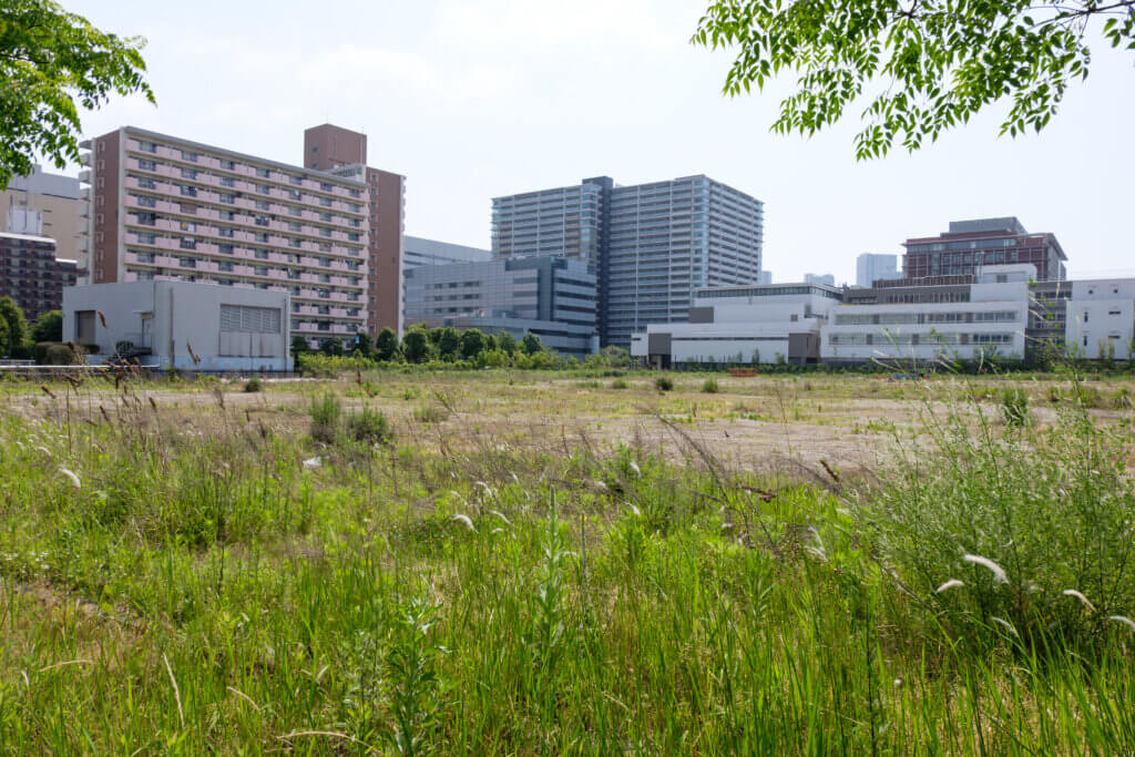 建物のない更地の区画と青空。奥に日本の住宅街