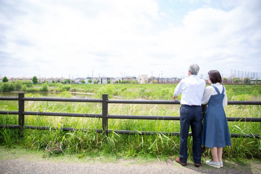 空き地に立って敷地を見ている日本人夫婦の後ろ姿、屋外