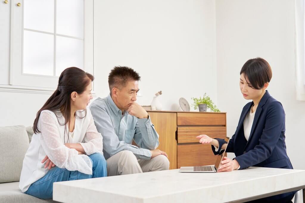 カウンターで資料を広げて相談する日本人夫婦と担当者、室内