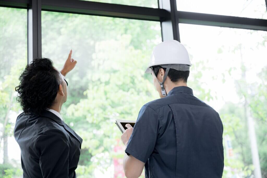 ヘルメット姿の日本人の担当者と施主が建築中の現場で話す